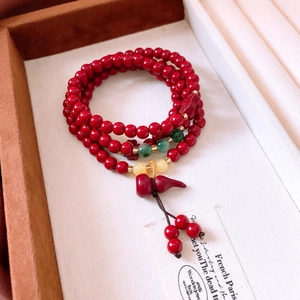 Macro shot of red cinnabar beads with green jade-like accents and a red gourd charm pendant