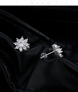 Macro shot of silver snowflake earrings with sparkling moissanite on black leather