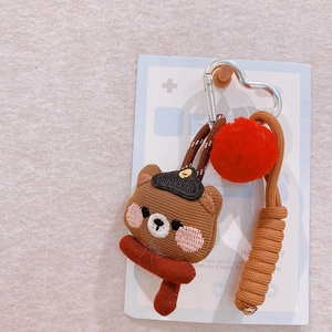 Detail of embroidered brown bear keychain with red scarf, pompom, and braided rope