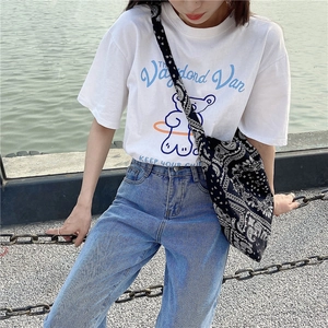 Close-up of white T-shirt with blue bear print paired with paisley canvas crossbody bag