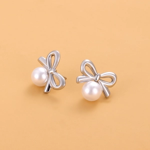 Gros plan de boucles d'oreilles nœud argenté avec perles blanches sur fond orange