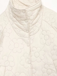 Close-up of floral quilted stitching and snap buttons on cream puffer jacket