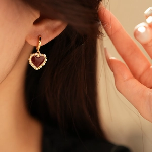 Dettaglio di orecchini a cuore dorati con pietre rosse e diamanti sulla modella donna