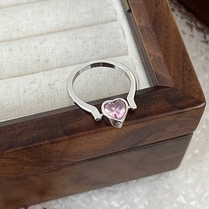 Macro view of a silver ring featuring a pink heart-shaped zircon on a wooden box