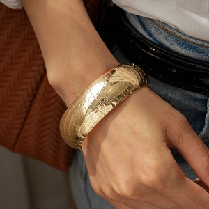 Macro detail of wide gold metal cuff bracelet featuring textured crocodile snake pattern
