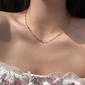 Detail of a dainty gold necklace featuring colorful gemstone beads on a model collarbone