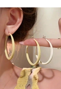 Close-up of large cream enamel hoop earrings worn by a model in a minimalist style