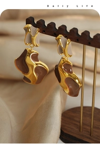 Close-up of irregular geometric gold-plated earrings with brown cow pattern enamel detail