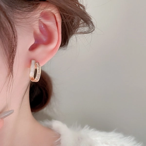 Detail of C-shaped gold plated earrings featuring shell inlay and sparkling crystals
