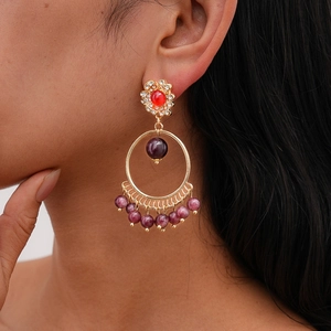 Detail of bohemian gold earrings featuring red gemstones and a large circular drop