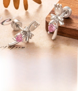 Macro detail of silver cartilage stud featuring pink heart zircon and bow tie charm