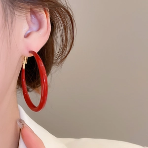Close-up of large red enamel hoop earring with polished gold finish on ear model