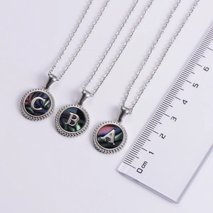 Detail of silver stainless steel pendant necklaces featuring shell inlay letters A B and C