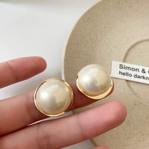 Detail of large round pearl stud earring with golden metal rim held by fingers