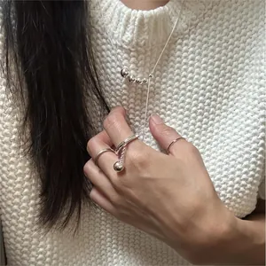 Detail of minimalist 925 silver beaded necklace and rings set on white knit background