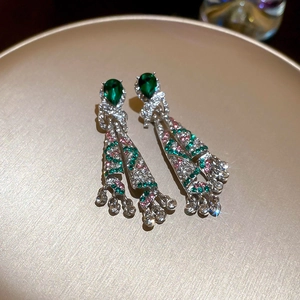 Macro view of silver tassel earrings with green and pink zircon stones on a gold tray