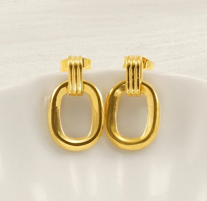 Close-up of golden oval drop earrings with striped texture on white porcelain container