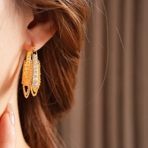 Close-up of gold chain fringe earrings with zircon inlay worn by model on brown background