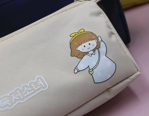 Dettaglio dell'astuccio in tela color crema con ragazza cartoon e scritte coreane