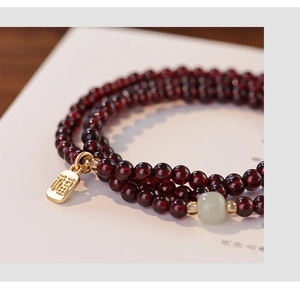 Macro detail of multi-layer garnet bead bracelet with jade bead and golden Fu charm