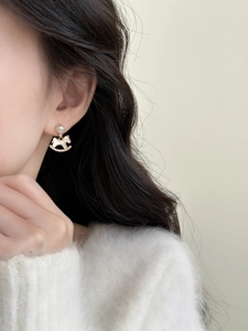 Close-up of golden rocking horse earrings with pearls and zircons worn by a model