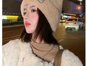 Detail of warm light brown knit beanie paired with a cozy winter faux fur coat in city night