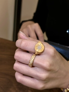 Detail of stacked 18K gold signet rings with star engraving and pavé diamond band textures
