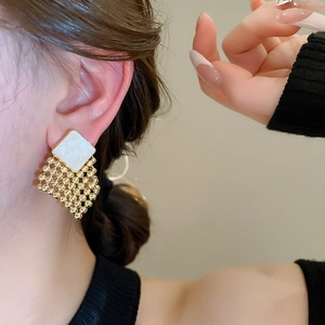 Close-up of geometric gold and white enamel rhombus stud earrings worn by a model