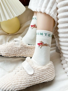 Close-up of white knitted socks featuring green WINTER text and a brown reindeer motif