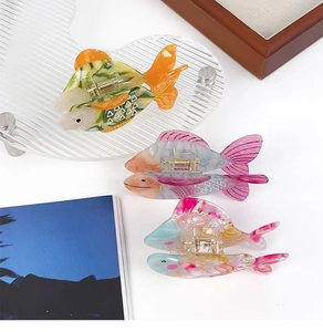 Close-up of three colorful acetate goldfish claw clips in yellow, pink and blue shades