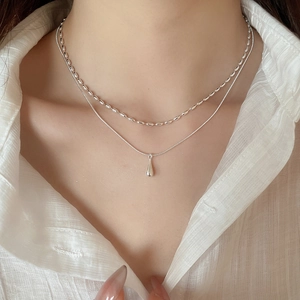 Close-up of double layer silver necklace with teardrop pendant worn on collarbone