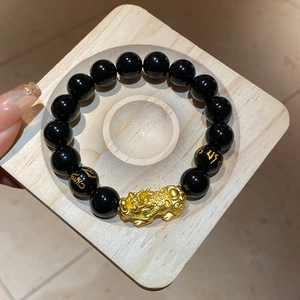 Macro detail of obsidian beads with golden Pixiu charm and engraved mantra symbols