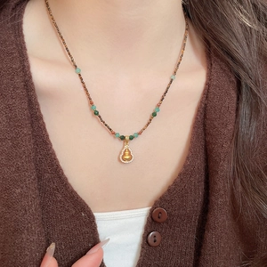 Close-up of golden gourd pendant with zircon inlay on brown beaded ethnic necklace