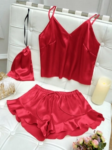 Red silk satin camisole pajama set with shorts and storage bag on white bench