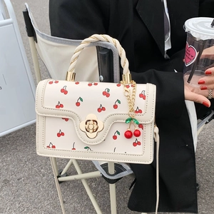 Creamy white crossbody bag with red cherry print, flower clasp, and woven handle