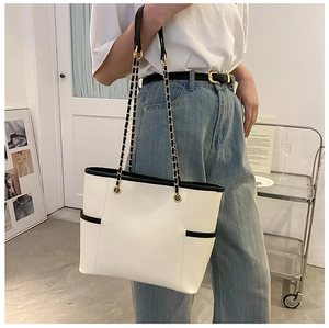 Detail of a beige tote bag with black piping and gold chain strap shown on a model