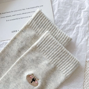 Detailed view of ribbed cuff and brown bear embroidery on off-white cotton socks