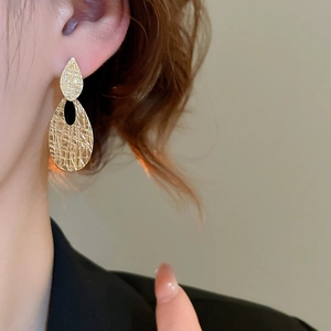 Detail showing gold teardrop earrings with textured hammered finish on a model