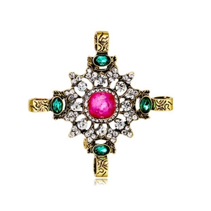 Macro shot of baroque cross brooch with pink gemstone and green crystal inlay details