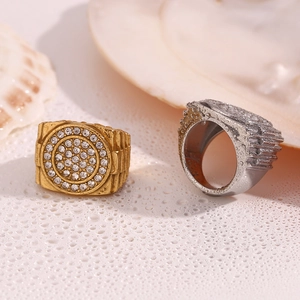 Close-up of gold and silver watch-band style rings with pavé set crystals on a wet surface