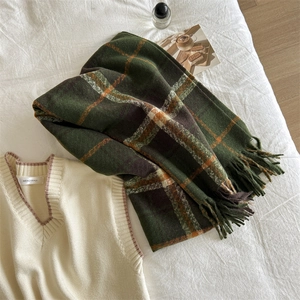 Detail of soft green plaid scarf with fringes styled with a sweater on white bedding