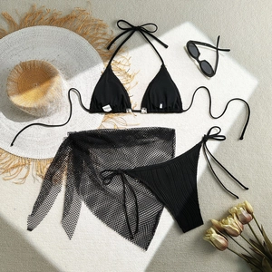 Flat lay of black 3-piece bikini set with mesh beach skirt and resort accessories