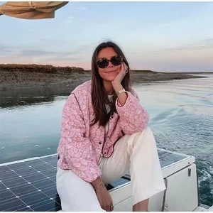 Pink paisley quilted jacket styled with white pants against a sunset waterfront background