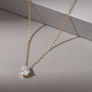 Detailed view of gold necklace with a round sparkling solitaire zircon in a four-prong setting