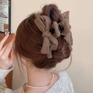 Detail view of a large dark brown fabric bow claw clip in a model hair styling scene