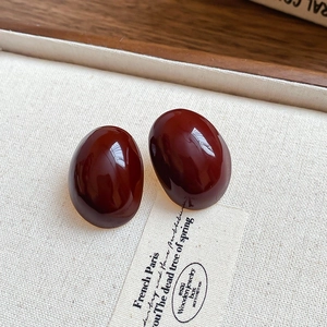Dettaglio di orecchini a perno ovali rosso scuro lucidi su vassoio in lino beige