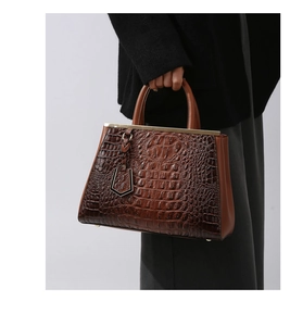 Detail of dark brown crocodile pattern leather handbag with gold metal bar hardware