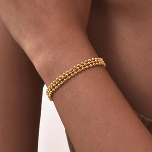 Close-up of triple-layered golden beaded bracelet on woman's wrist showing detailed texture