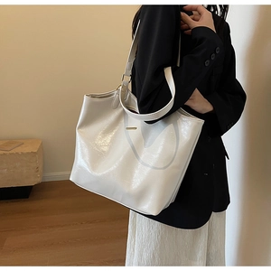 Close-up of white glossy patent leather tote bag with fine straps worn by a model