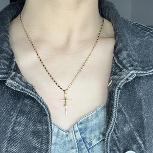 Close-up of a gold cross necklace with pavé zircon stones on a square link chain